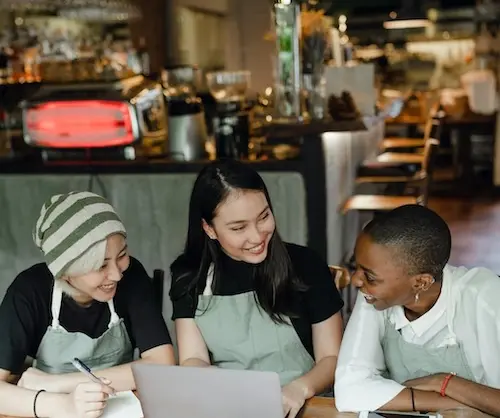 Three people working on laptop in cafe